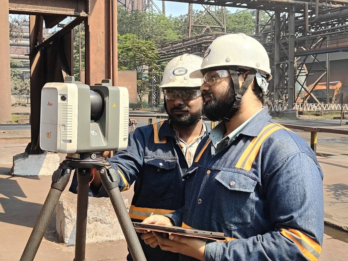 Two VB engineers in hard hats operating a Leica laser scanner and tablet in a plant yard