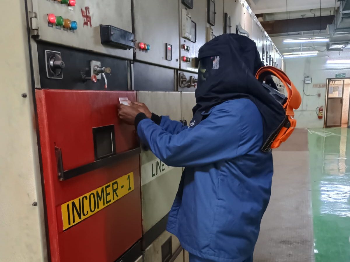 VB engineer in an arc flash suit and hood applying a label to an incomer panel