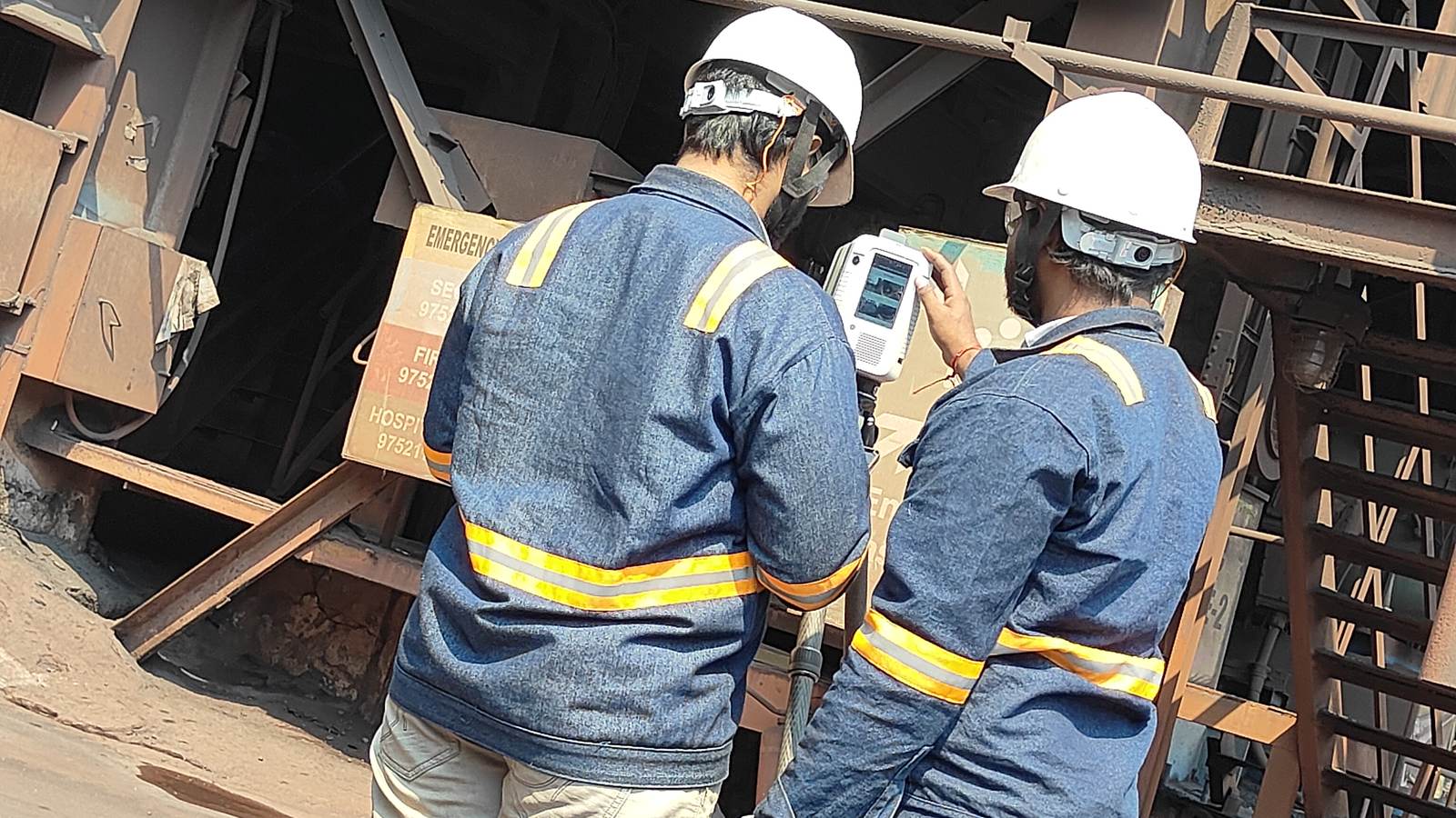 Two VB engineers in hi-vis at a Leica laser scanner on site, seen from behind
