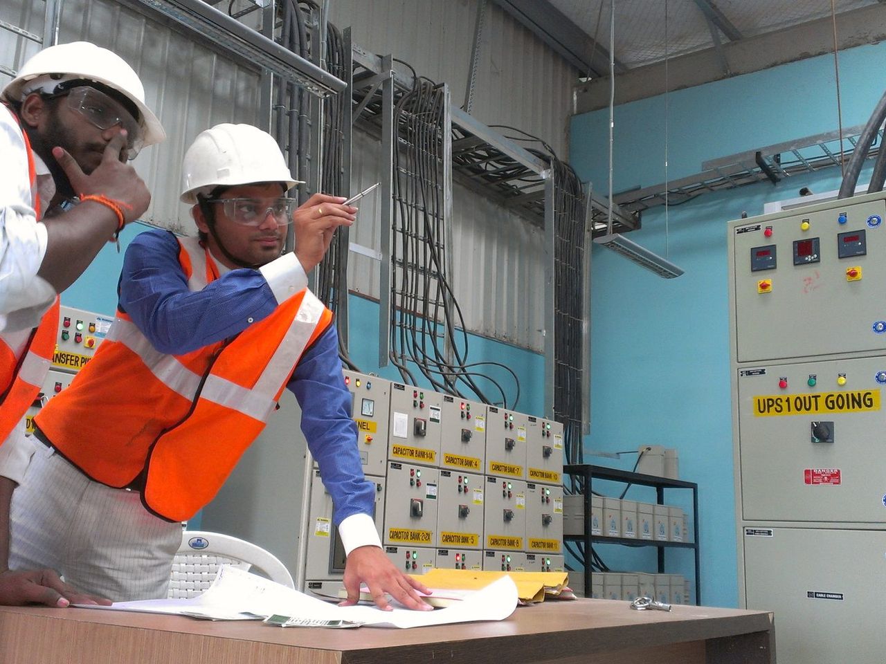 Two VB engineers reviewing drawings beside UPS outgoing feeder panels during an arc flash study walkdown