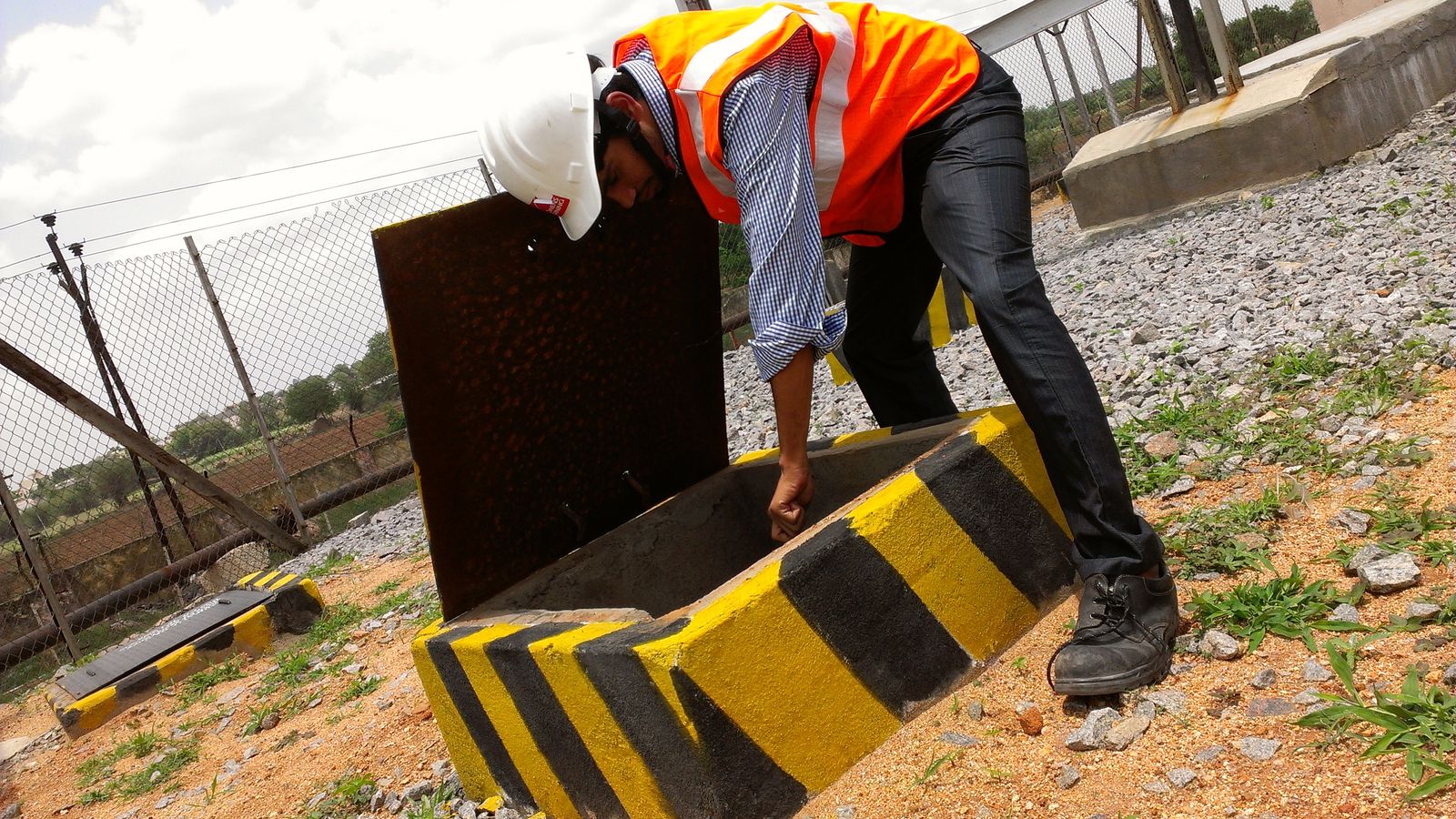 VB engineer lifting the cover of an earth pit chamber at an outdoor substation to inspect the electrode and connection