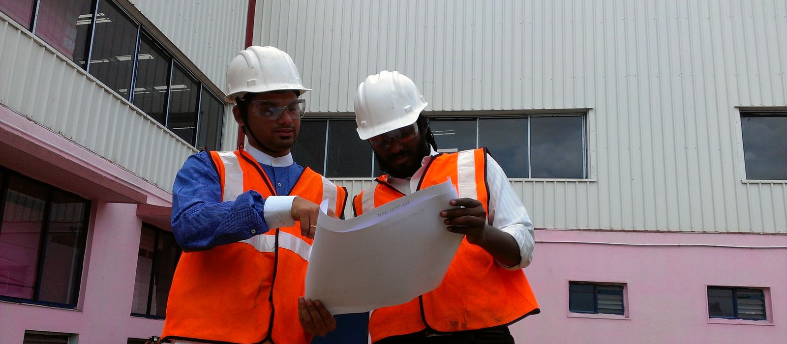 Two VB engineers outside a plant building checking the site layout drawing against the structure in front of them