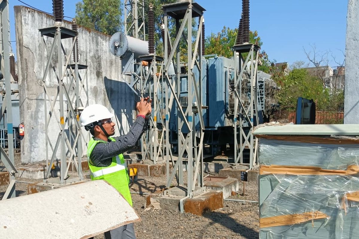 VB engineer in hard hat and hi-vis photographing masts and structures in an outdoor switchyard