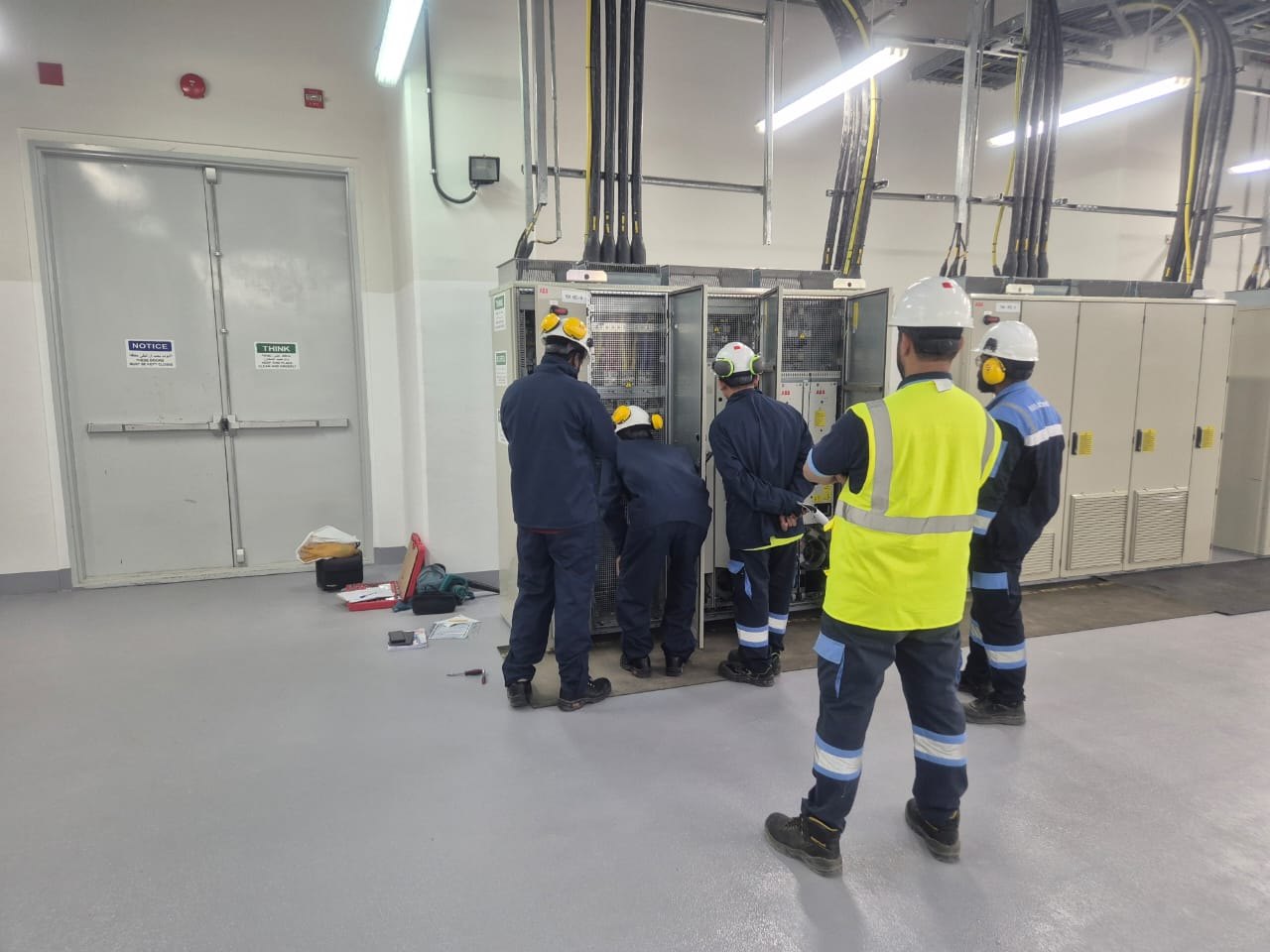 VB survey crew in arc-rated coveralls and hard hats recording panel data at an open switchgear lineup