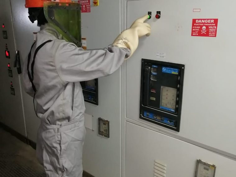 Worker in an arc flash coverall, face shield and gloves standing at an energised low voltage panel