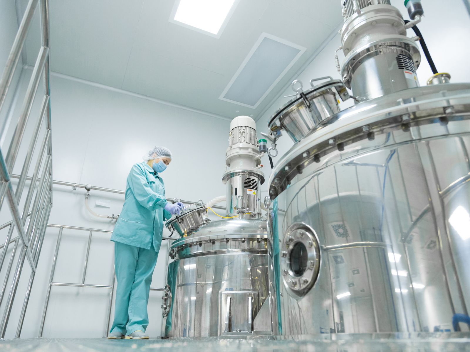 A worker in a cleanroom suit operating stainless steel process equipment