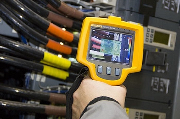 Hand-held thermal imager pointed at cable terminations and breakers inside an open LT panel